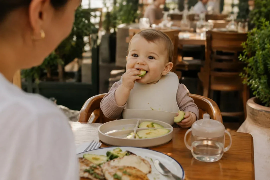 Baby eating avocado at a restaurant while starting solids with family