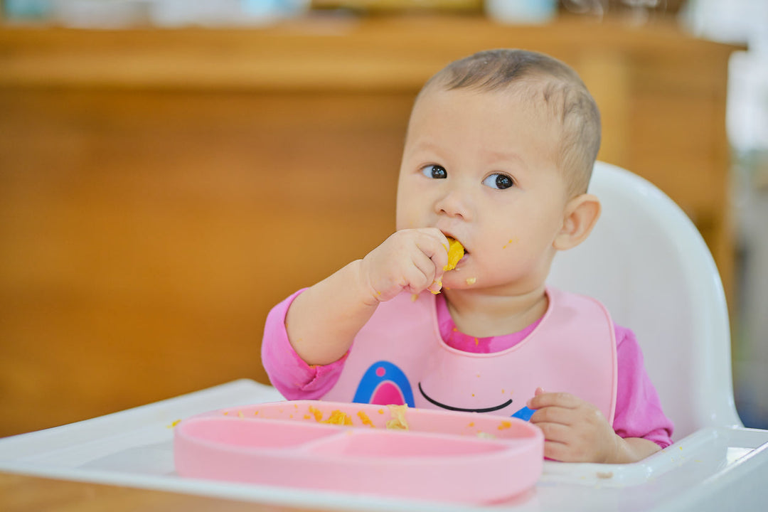 Baby sitting upright in high chair practicing baby-led weaning with soft finger food
